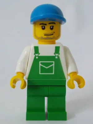 Groene overall met zak, groene broekspijpen, blauwe pet met korte gebogen klep, grijns en stoppelbaard.